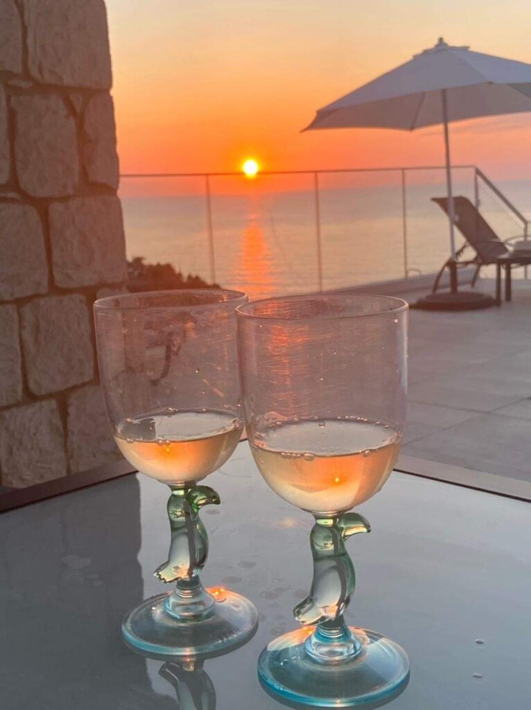 Two glasses on table, sunset over ocean view.